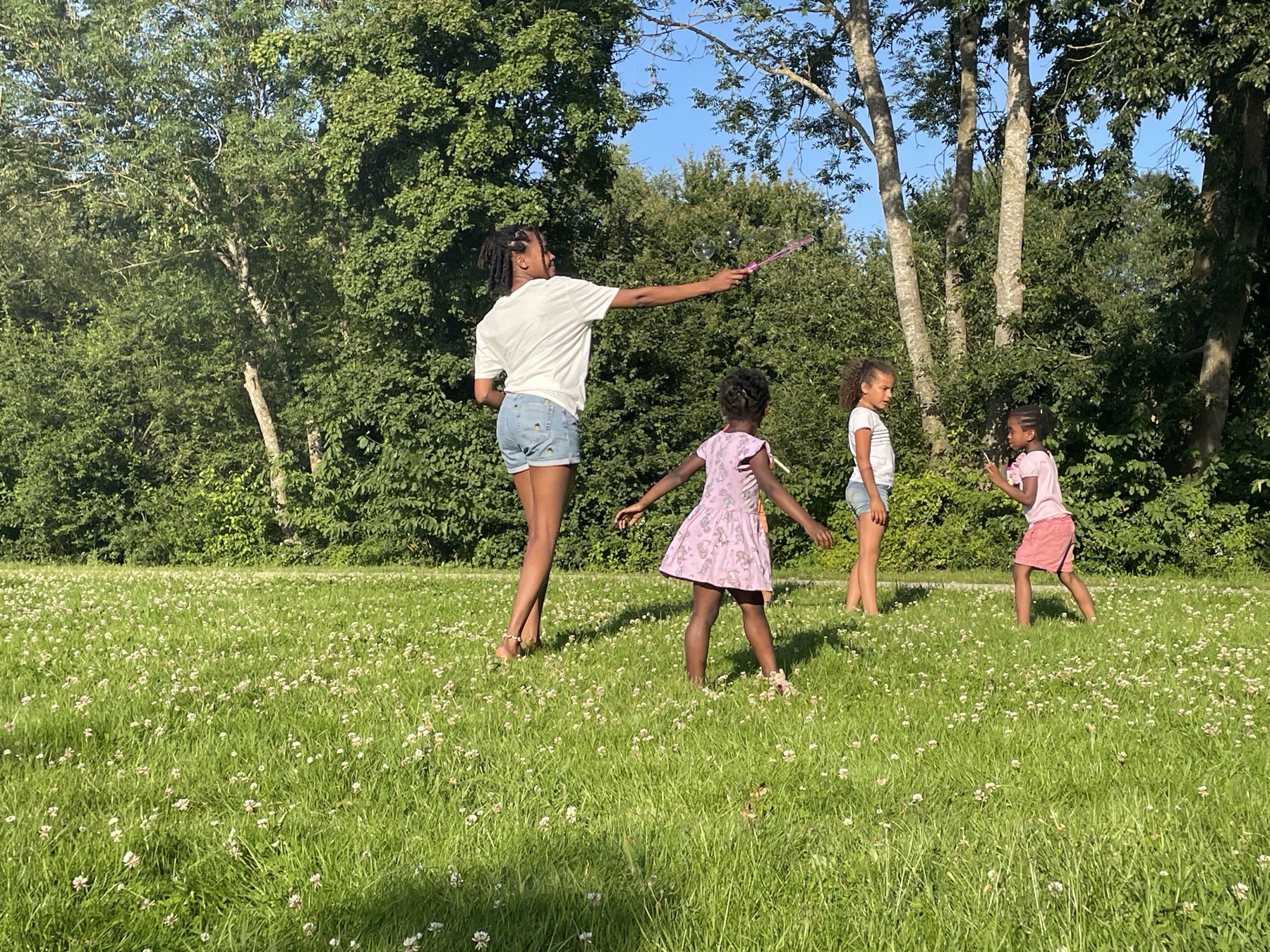 Fatima-Marie spielt mit Kindern Seifenblasen auf einer Sommerwiese